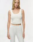 Woman wearing a white ribbed tank top and white pants on a plain background