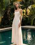 Woman in a white dress standing by a pool with lush greenery in the background
