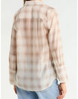 A woman shown from the back wearing a semi-sheer long-sleeve button-up shirt with a beige and light brown plaid pattern, paired with light blue jeans, against a plain white background.