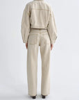 A model shown from the back wearing a light beige cropped denim jacket and matching wide-leg denim jeans against a plain light gray studio background.