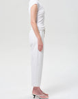 A model shown in profile wearing a white short-sleeve top, white cropped pants, and light pink heeled sandals against a plain light gray studio background.