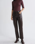A model wearing a dark burgundy mock-neck long-sleeve top, dark brown leather-look straight-leg pants, and dark brown heeled ankle boots, standing against a light gray studio background.