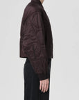 Person wearing a dark quilted jacket on a light gray background, side