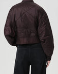 Person wearing a dark brown quilted jacket on a white background, back