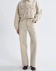 A model wearing a light beige cropped denim jacket and matching wide-leg jeans, paired with dark brown shoes, against a plain light gray studio background.