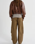 A model shown from the back wearing a brown faux-leather bomber jacket, a light gray t-shirt, and wide-leg brown cargo pants against a plain white studio background.