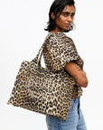 Person wearing a leopard print top and holding a matching bag on a white background