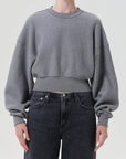 Person wearing a gray cropped sweatshirt and dark jeans on a plain background