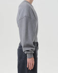 Person wearing a gray sweatshirt and dark jeans on a light gray background, side