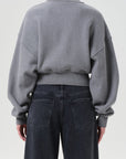 Person wearing a gray sweatshirt and dark jeans on a plain background, back