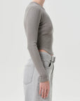 Person wearing a gray long-sleeve top and light gray jeans on a white background, side