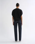 A model shown from the back wearing a black short-sleeve top and dark blue straight-leg jeans against a plain white studio background.