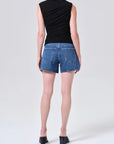 model wearing denim shorts with black shirt and heels on a white background, back view
