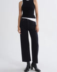 A model wearing a black sleeveless ribbed top with white shoulder panels, black wide-leg cropped pants, and black heeled ankle boots, photographed against a light gray studio background.