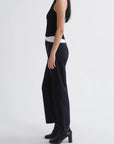A model shown from the side wearing a black sleeveless top, wide-leg navy trousers, and black ankle boots against a plain light gray studio background.
