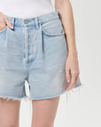 model wearing light wash denim shorts with a white top on a white background