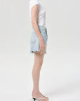 model wearing light wash denim shorts with a white top on a white background, side view