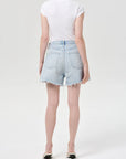 model wearing light wash denim shorts with a white top on a white background, back view