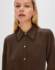 Woman wearing a brown blouse with a high collar on a white background