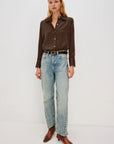 Woman wearing a brown shirt, light blue jeans, and brown shoes on a white background