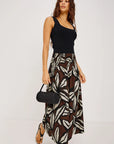 Woman wearing a black top and patterned skirt holding a black handbag on a white background