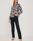 Woman wearing a patterned blouse and dark jeans on a white background