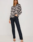 Woman wearing a patterned blouse and dark jeans on a white background
