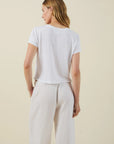 Woman wearing a white t-shirt and light-colored pants against a beige background