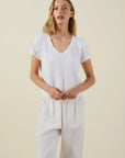 Woman wearing a white t-shirt and light-colored pants against a beige background