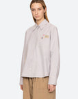 Person wearing a light gray shirt with embroidered patches on a white background