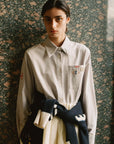Person wearing a light-colored shirt with embroidered details against a textured wall.