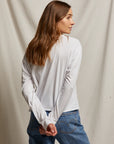 Woman wearing a white long-sleeve shirt and blue jeans against a plain background, back view, size S