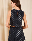 model wearing a dark colored top and skirt set with metallic polka dots on a cream background, back view