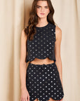 model wearing a dark colored top and skirt set with metallic polka dots on a cream background