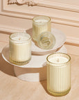 Three Champs de Tuberose Candles in glass holders on a decorative stand against a beige wall.