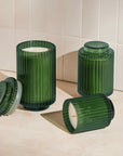Green ribbed candle holders with candles on a tiled floor.