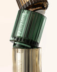 Perfume bottle with green cap and gold body on a beige background