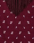 Close-up of a burgundy fabric with a fringe neckline and small white and blue floral embroidered motifs.