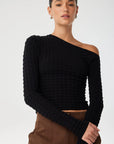 Woman wearing a black one-shoulder sweater against a white background