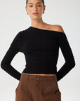 Woman wearing a black off-shoulder top and brown pants on a white background