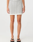 Person wearing a white skirt with black wavy pattern on a plain background