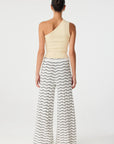 Woman wearing a one-shoulder top and wavy patterned pants on a white background