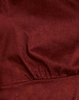 A close-up of a dark red or burgundy textured fabric with soft folds and a gathered seam.