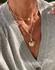 Close-up of a person wearing a gold chain necklace with a heart pendant.