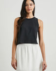 Woman wearing a black sleeveless top and white skirt against a plain background