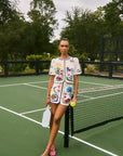 Woman in a floral outfit standing on a tennis court holding a racket and a ball.