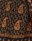 A close-up of a black fabric printed with a repeating tan paisley and floral block pattern, including a decorative border along the bottom edge.