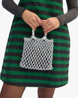 Person holding a silver mesh handbag against a green and black striped dress.