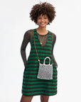Woman wearing a green and black striped dress holding a silver bag on a white background