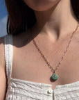 Necklace with a green pendant worn by a person against a blue sky.
